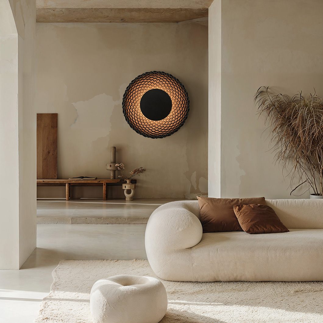 Large round wall light made from black quartz sand casting a soft, warm glow alternative image